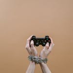 Conceptual image of hands in chains holding a game controller symbolizing gaming addiction.